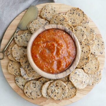 bowl of dip surrounded by seed crackers on a circular wooden serving board