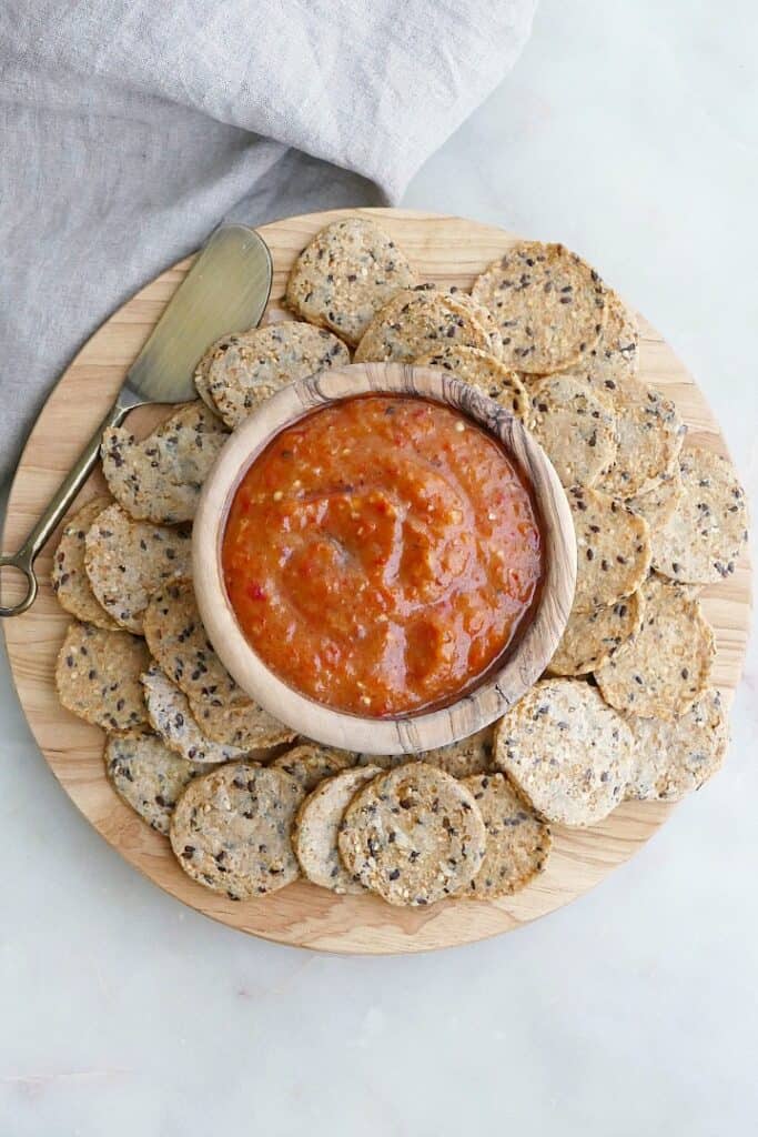 bowl of dip surrounded by seed crackers on a circular wooden serving board