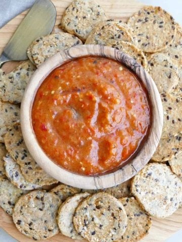 square image of eggplant red pepper dip surrounded by seed crackers on a serving platter