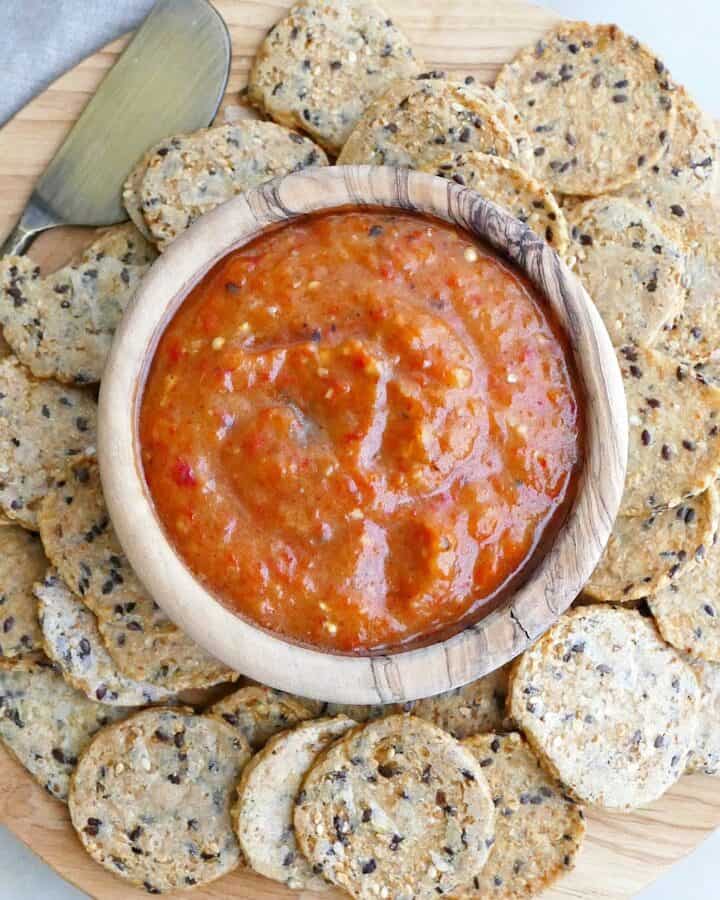 square image of eggplant red pepper dip surrounded by seed crackers on a serving platter