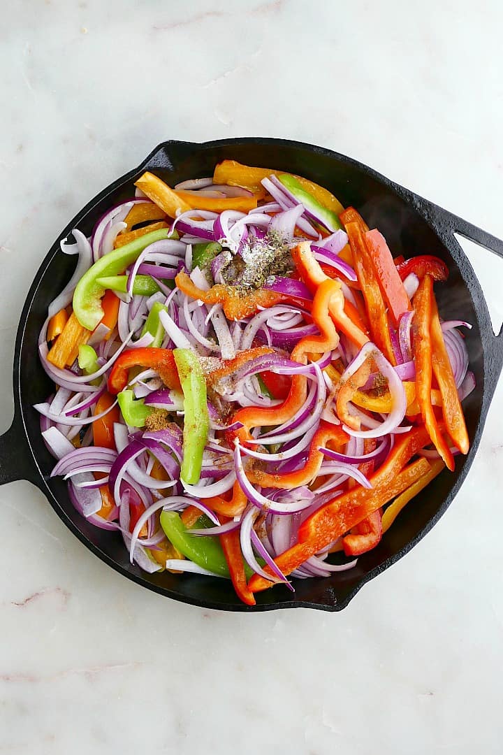 sliced peppers and onions dusted with seasonings in a large cast iron skillet