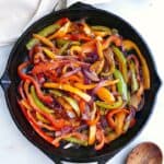 cooked fajita veggies in a cast iron skillet next to a spoon and napkin