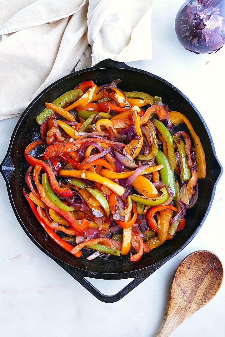 cooked fajita veggies in a cast iron skillet next to a spoon and napkin