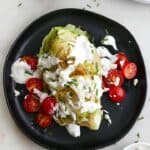 wedge salad with blue cheese dressing and cherry tomatoes on a black plate