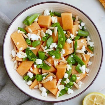 melon and sugar snap pea salad in a bowl next to a lemon and napkin