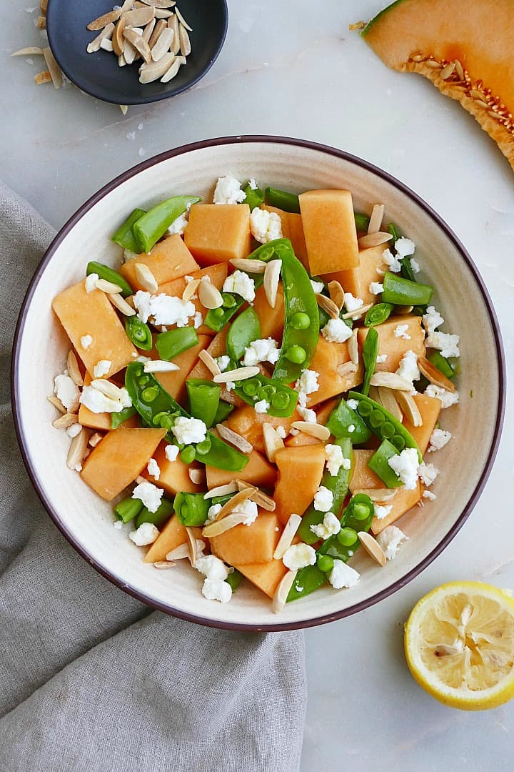 melon and sugar snap pea salad in a bowl next to a lemon and napkin