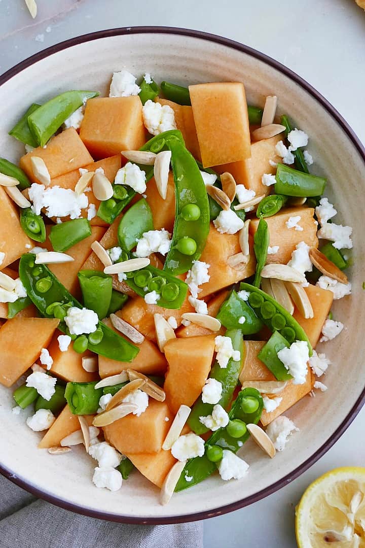 sugar snap pea, cantaloupe, slivered almonds, and goat cheese in a bowl on a counter