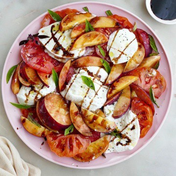 peach caprese salad drizzled with balsamic and garnished with basil on a platter