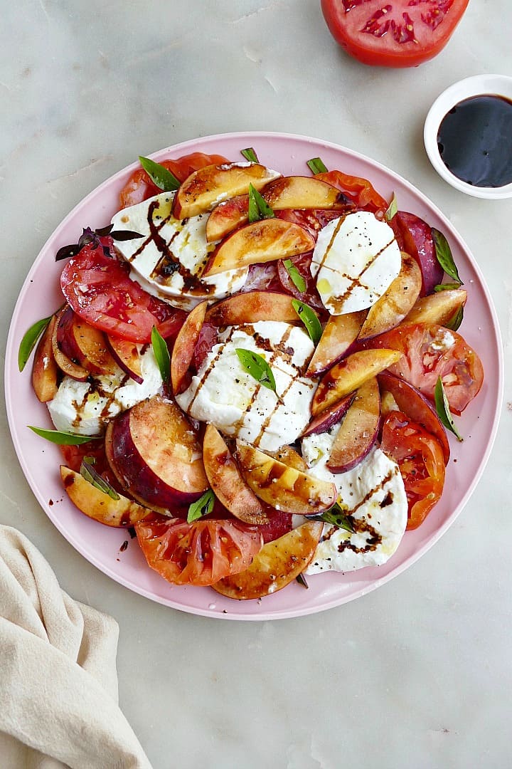 peach caprese salad drizzled with balsamic and garnished with basil on a platter