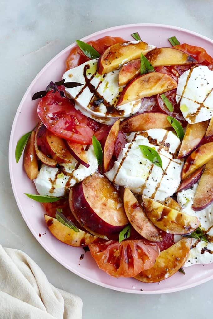 close-up of peach caprese salad garnished with balsamic and basil on a counter