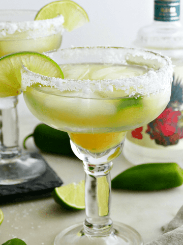 pineapple jalapeno margaritas on a counter garnished with salt rims and lime