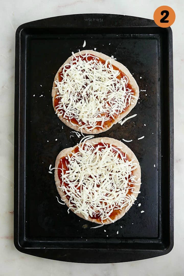 whole wheat pitas on a baking sheet spread with barbecue sauce and cheese