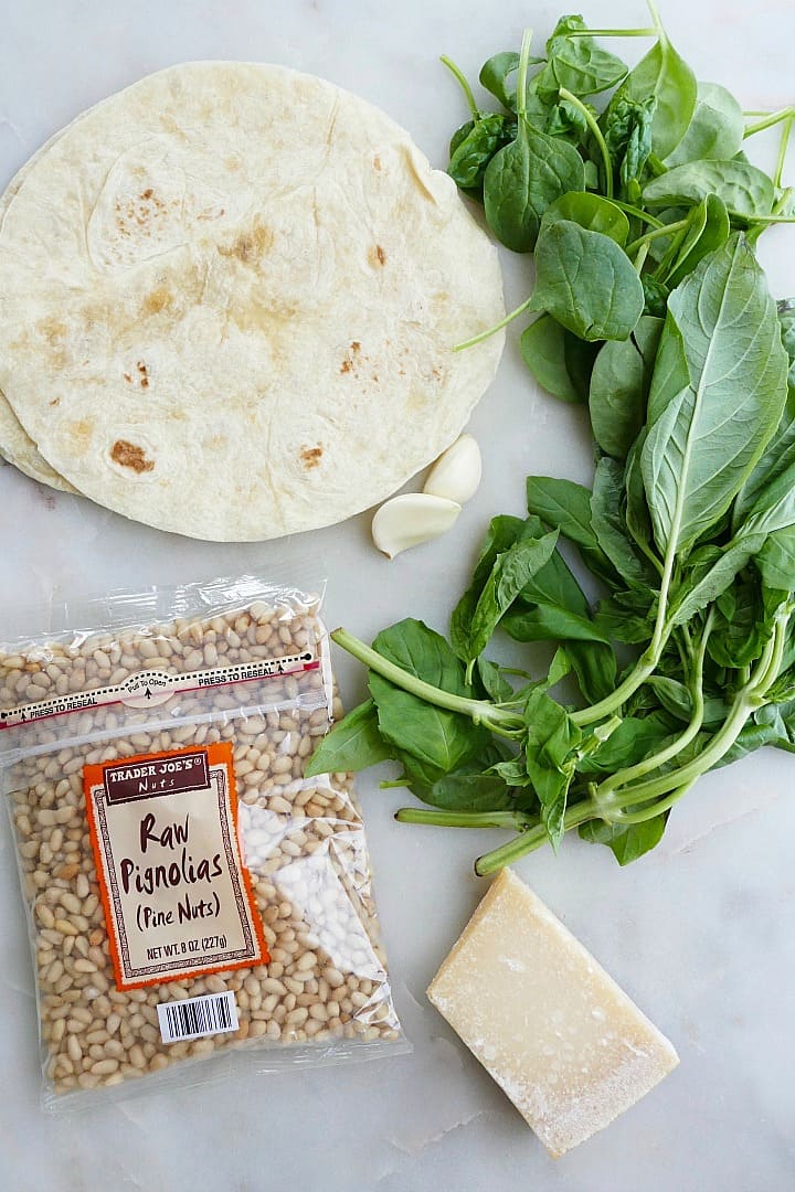 flour tortillas, pine nuts, parmesan cheese, and basil on a counter