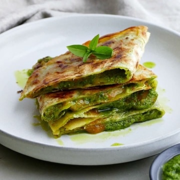 sliced quesadilla stacked on top of each other on a plate with basil leaves on top