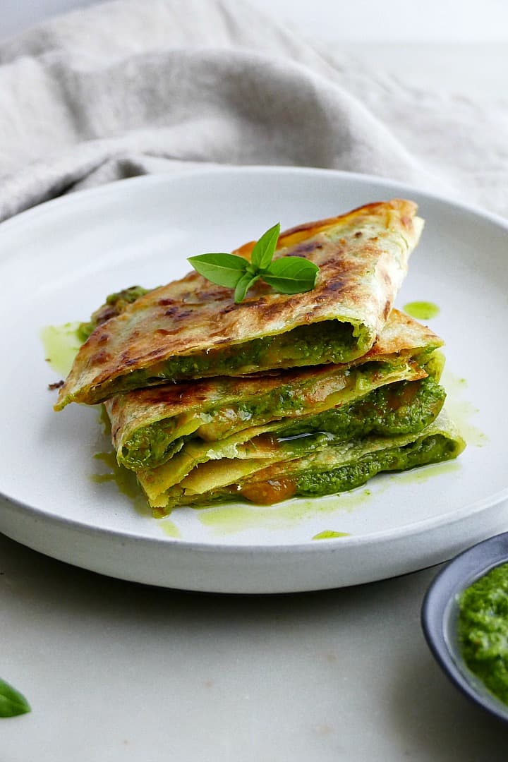 sliced quesadilla stacked on top of each other on a plate with basil leaves on top