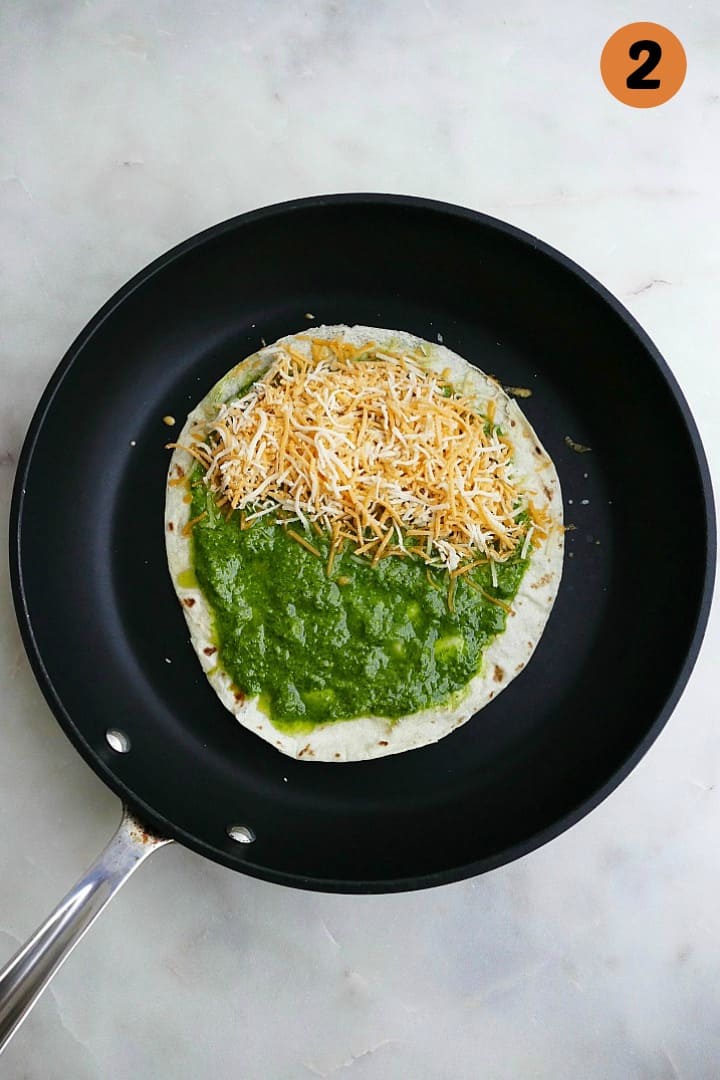 quesadilla spread with pesto and cheese in a black skillet on a counter