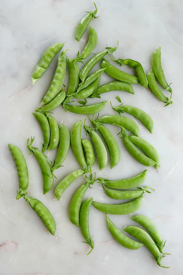 freshly picked sugar snap peas spread out on a white counter