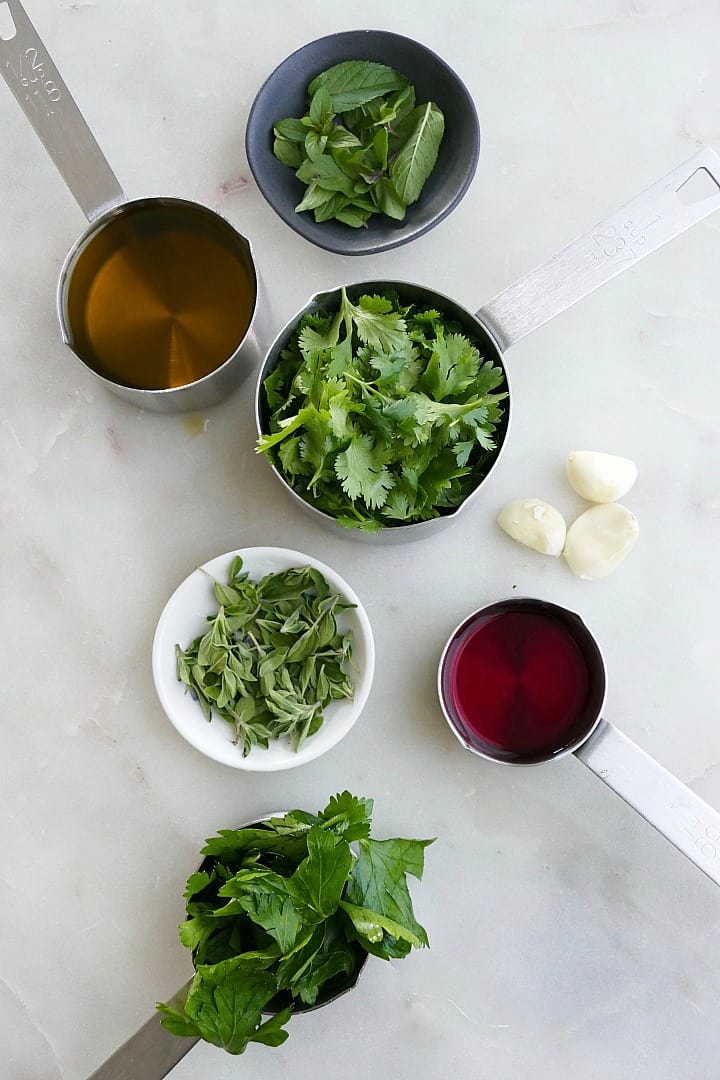 cilantro, mint, parsley, oregano, olive oil, red wine vinegar, and garlic on a counter