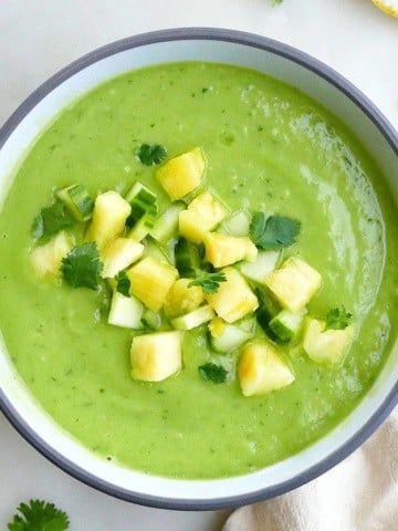 square image of a cucumber avocado soup with chopped pineapple on a counter