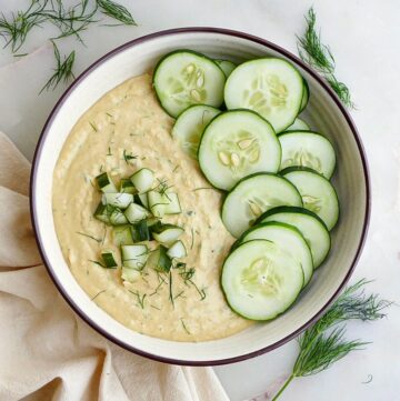 dill pickle hummus in a serving bowl garnished with cucumber slices