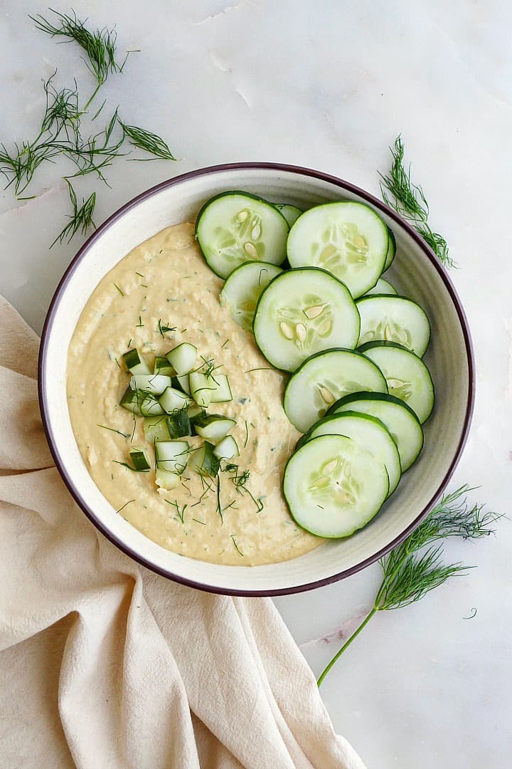 dill pickle hummus in a serving bowl garnished with cucumber slices