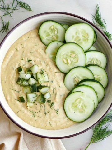 square image of dill pickle hummus garnished with cucumbers and dill