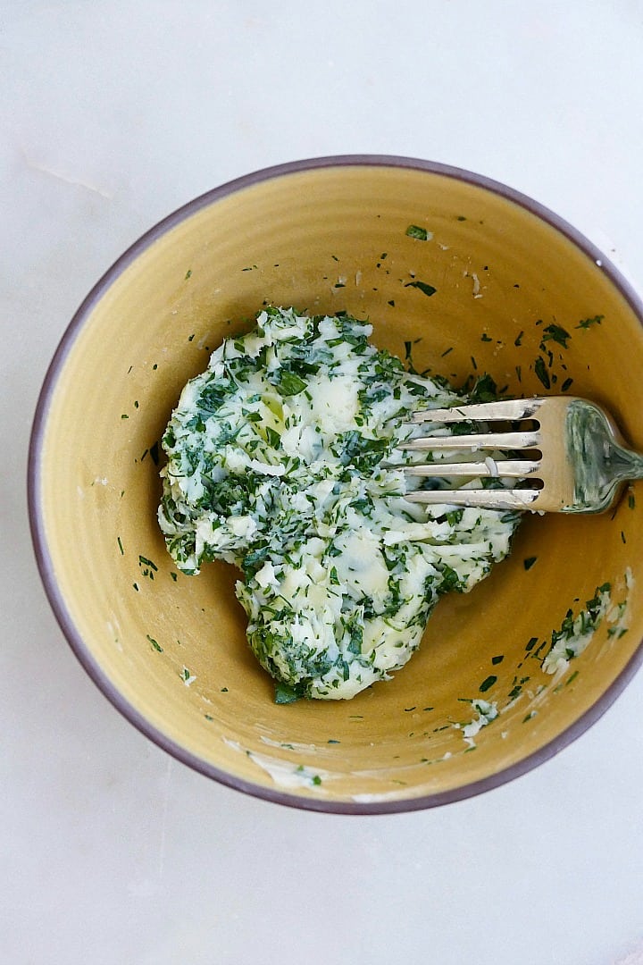 garlic and herb butter mixed together with a fork in a yellow bowl