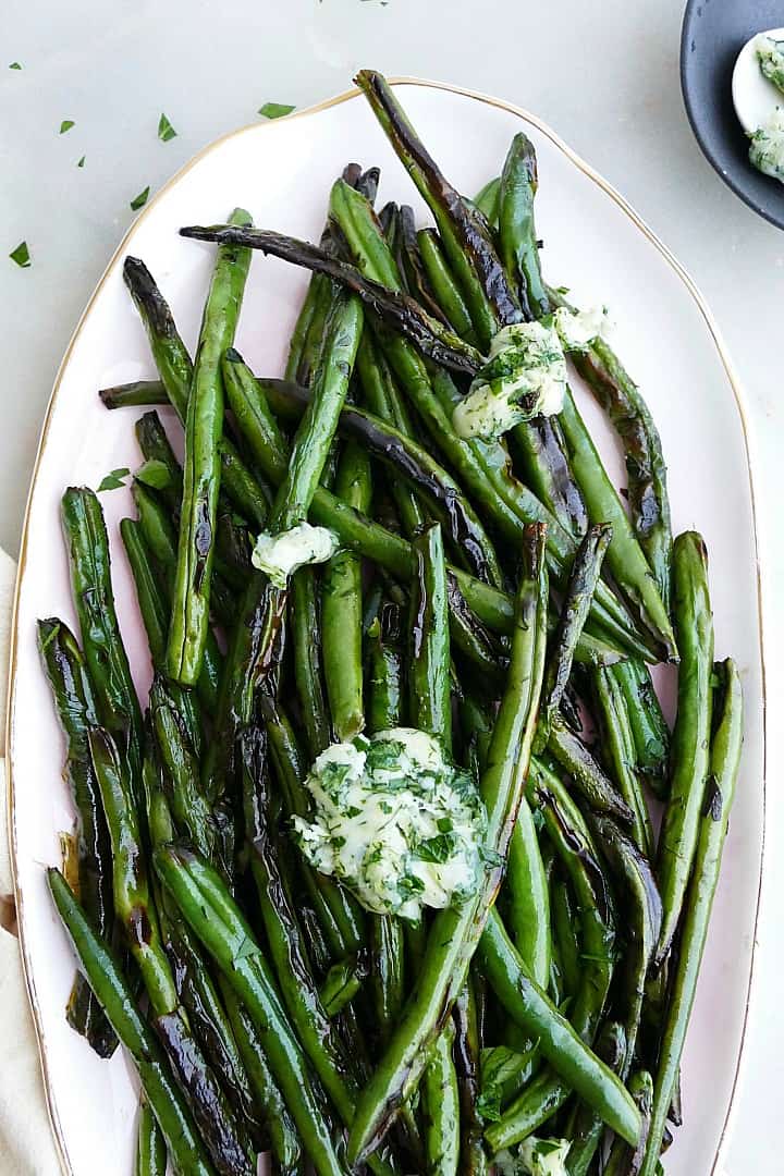 close up of garlic butter green beans on a serving platter topped with butter