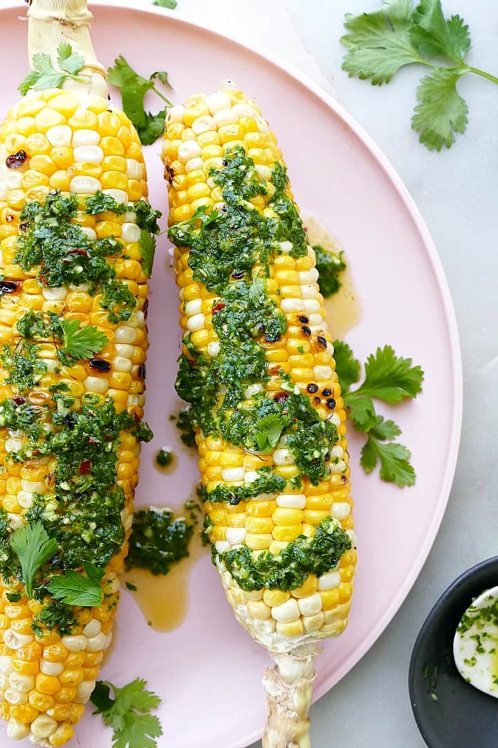 grilled sweet corn cobs with cilantro chimichurri on a pink serving platter