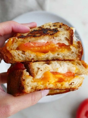 square image of grilled cheese sandwich cut in half in a hand