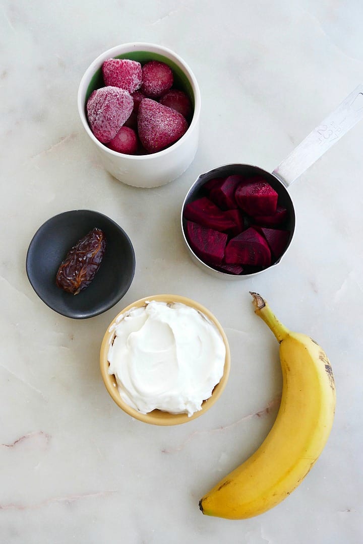 frozen strawberries, diced beets, date, yogurt, and banana next to each other on a counter