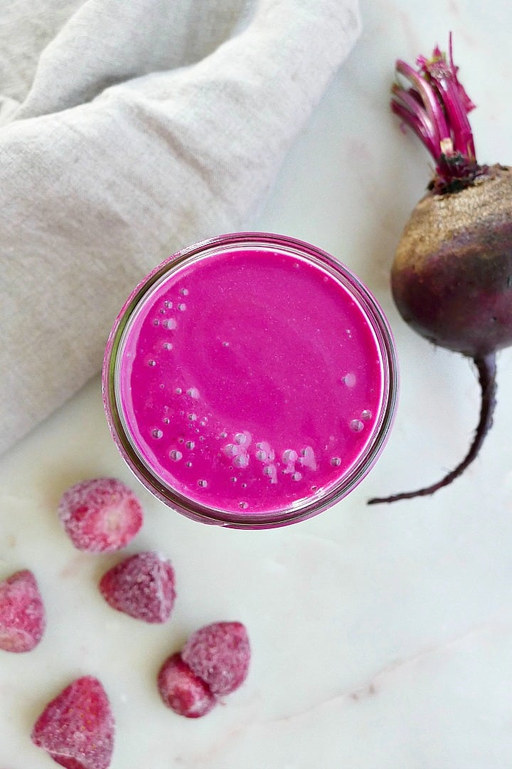 strawberry banana beet smoothie on a counter next to ingredients and a napkin