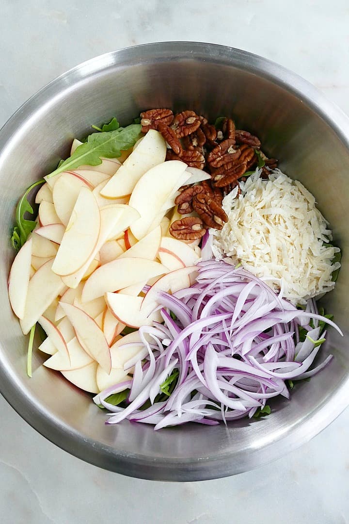 sliced apples and red onions, shredded parmesan, pecans, and arugula in a mixing bowl