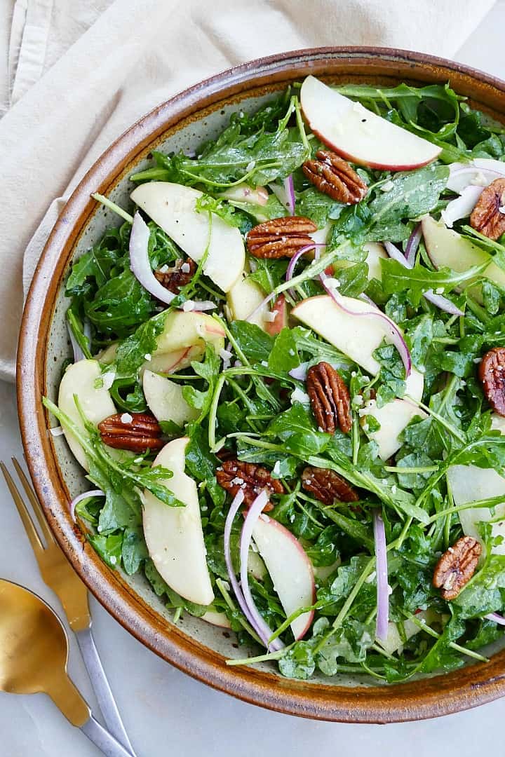 close image of arugula salad with apples and pecans on a counter