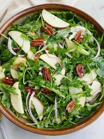 square image of arugula apple salad in a large serving bowl on a counter
