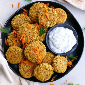 several carrot falafel patties on a serving dish with homemade tzatziki sauce