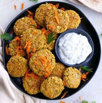 several carrot falafel patties on a serving dish with homemade tzatziki sauce