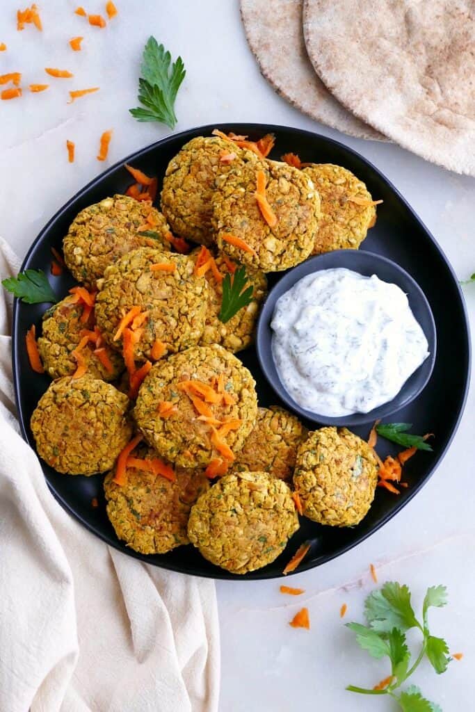 several carrot falafel patties on a serving dish with homemade tzatziki sauce
