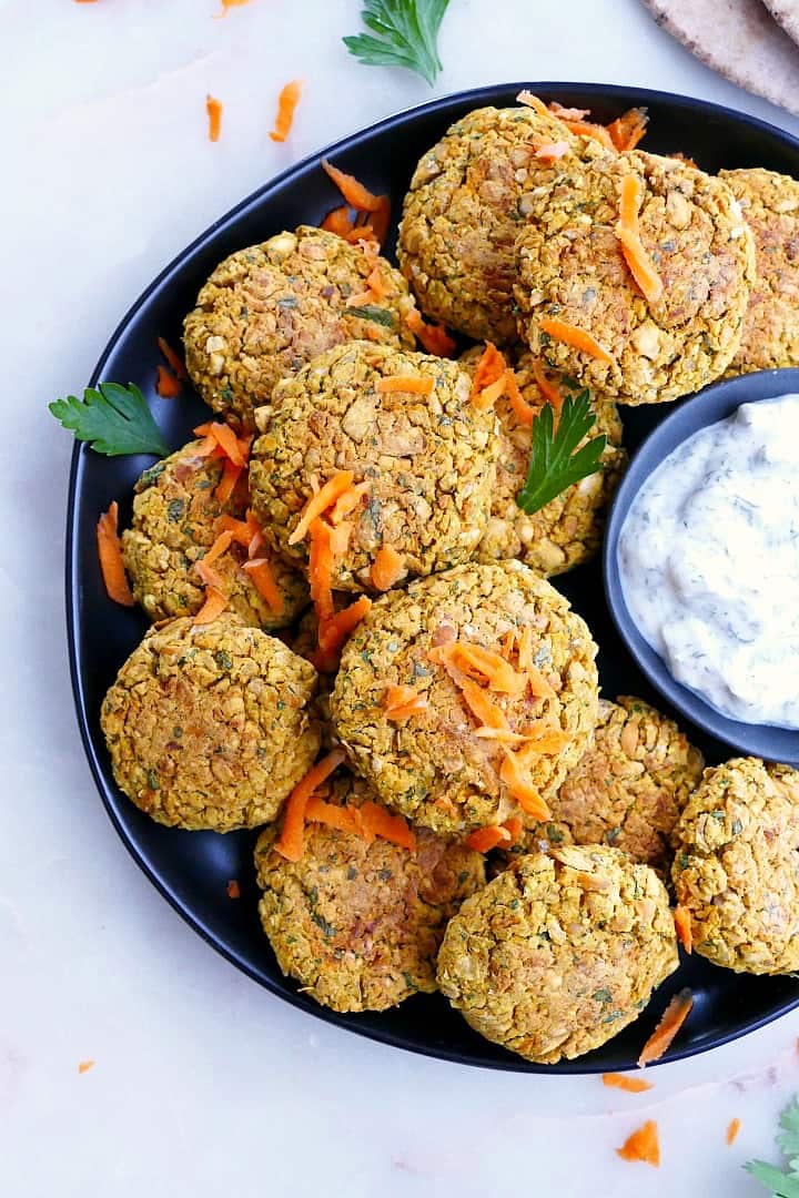close up of baked falafel patties on a serving platter with grated carrots and cilantro