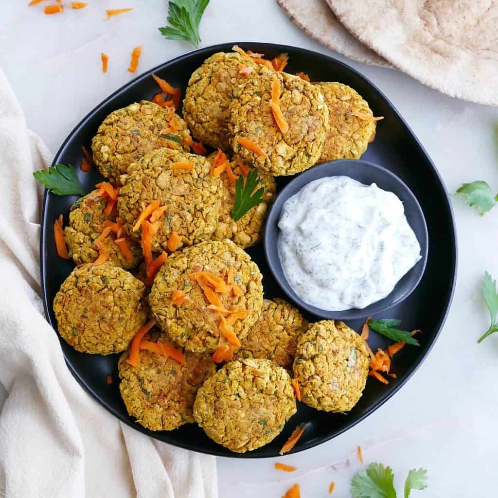 square image of baked curry carrot falafel on a platter with tzatziki