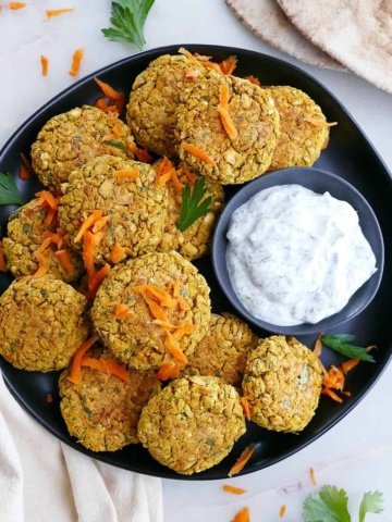 square image of baked curry carrot falafel on a platter with tzatziki