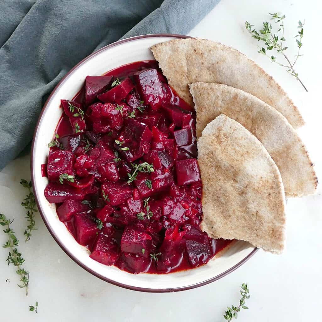 square image of beetroot curry and pita slices in a serving bowl