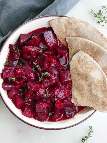 square image of beetroot curry and pita slices in a serving bowl
