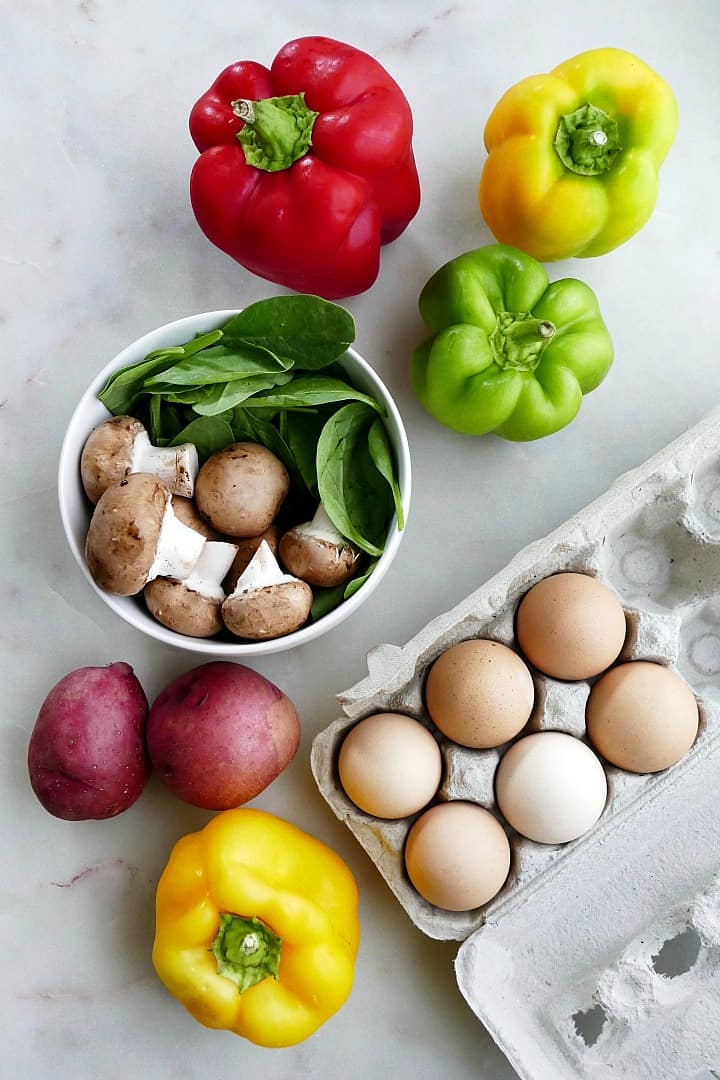 bell peppers, mushrooms, spinach, potatoes, and eggs spread out on a counter