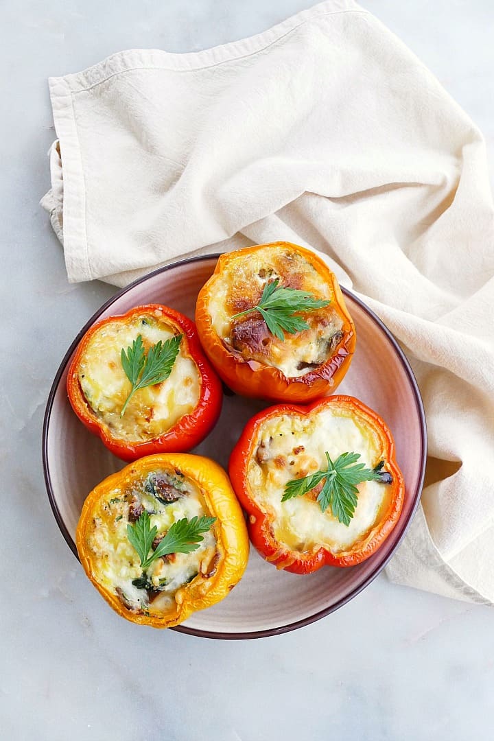 four breakfast stuffed bell peppers topped with cheese and parsley on a serving platter