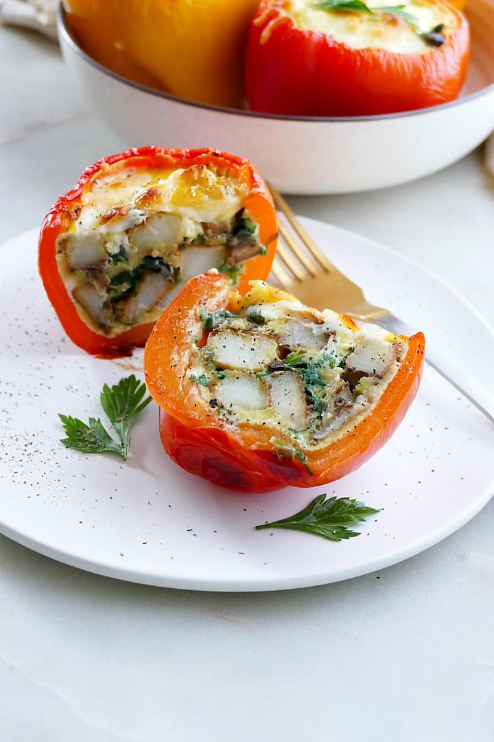 potato and egg stuffed pepper sliced in half on a plate with a fork behind it