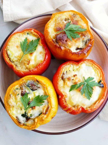 square image of four breakfast stuffed bell peppers topped with cheese and parsley on a serving platter