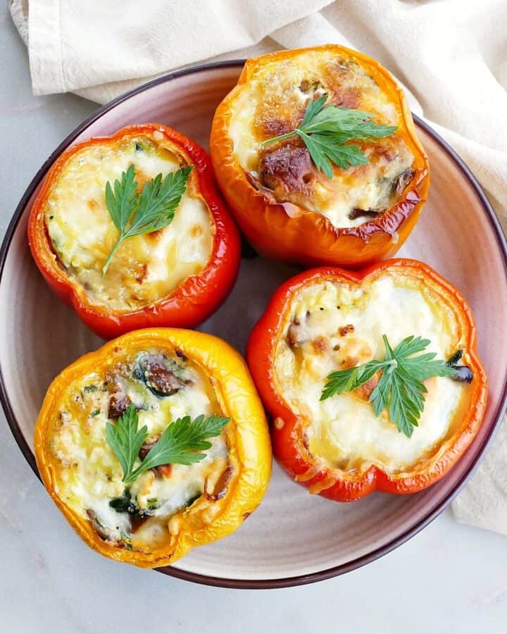 square image of four breakfast stuffed bell peppers topped with cheese and parsley on a serving platter