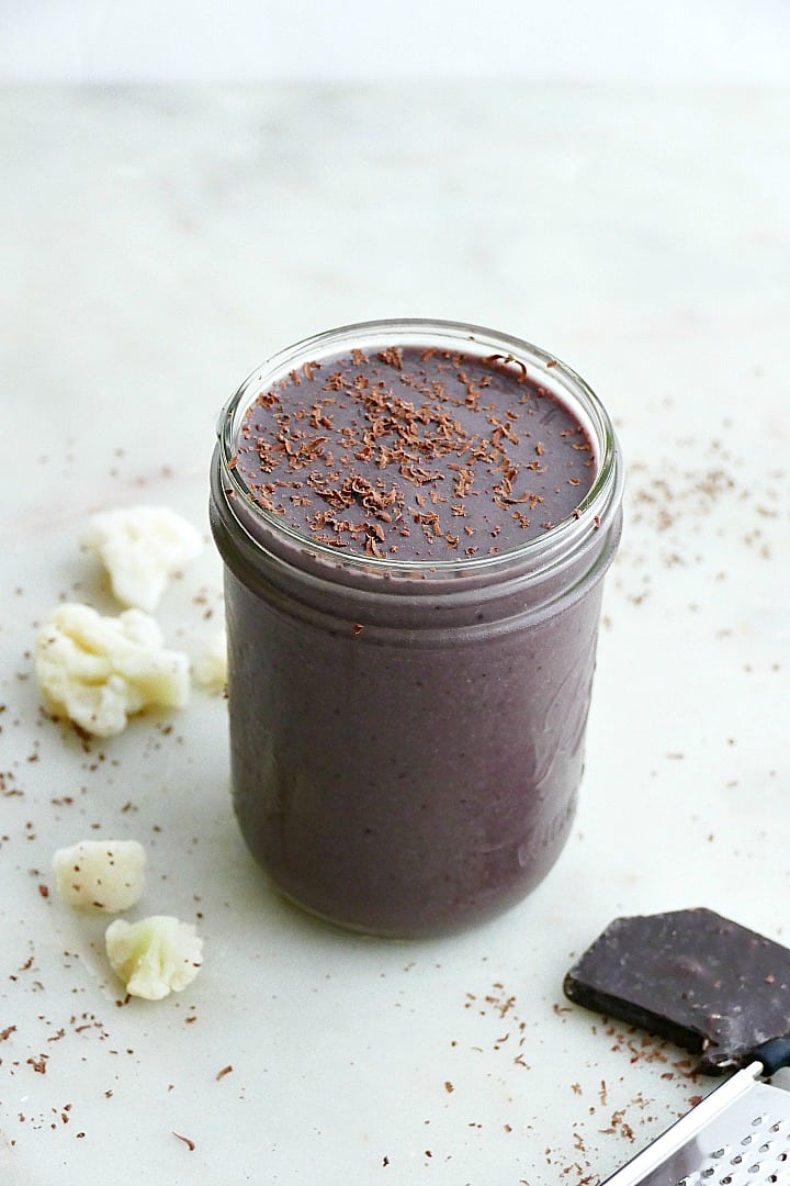 side view of purple cauliflower smoothie next to frozen cauliflower and chocolate