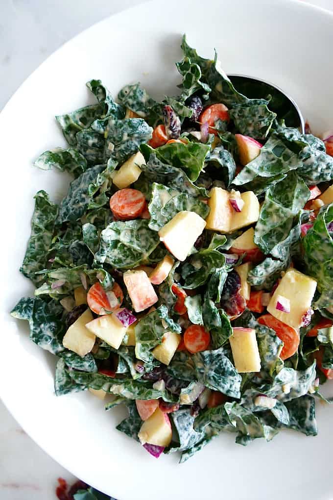 kale, apple, carrot, and dried cranberry salad in a large mixing bowl with a spoon